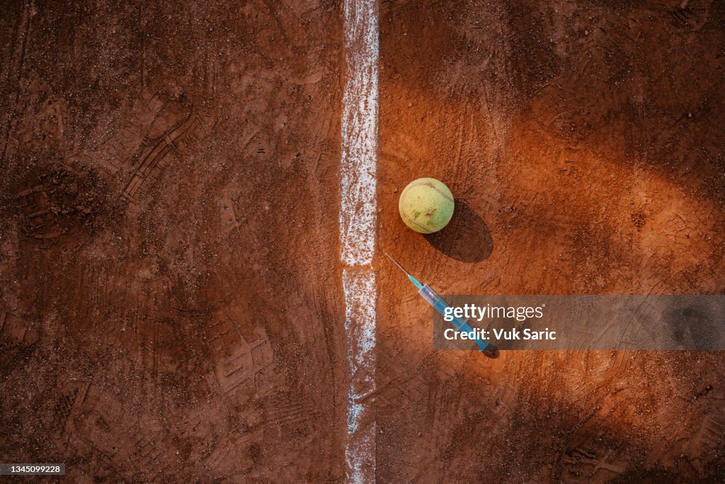 Tennis ball and syringe for vaccine next to a baseline