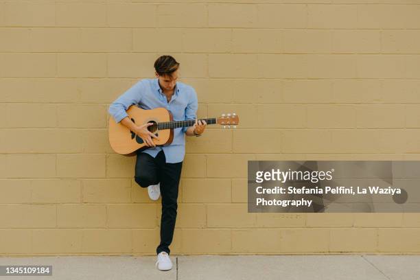 teenager boy leaning against a wall while playing the guitar - acoustic guitarist stock pictures, royalty-free photos & images