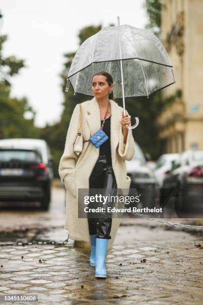 Julia Comil wears earrings, a black V-neck tank-top, black shiny leather pants, a white latte sheep long fluffy oversized coat, a blue shiny leather...