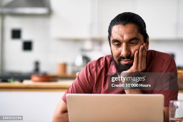 mid adult man using laptop in kitchen - hand on chin stock pictures, royalty-free photos & images