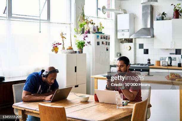 mid adult men working at home from kitchen table - roommate fotografías e imágenes de stock