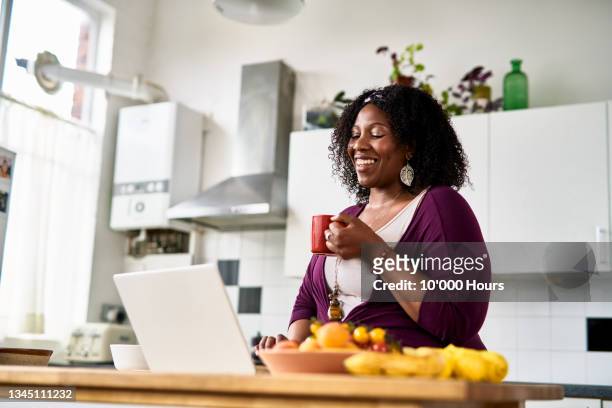 cheerful mid adult woman using laptop and smiling in online meeting - woman portrait kitchen laptop bildbanksfoton och bilder