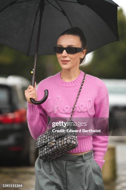 Mary Leest wears sunglasses, a pink wool with fluffy embroidered Chanel inscriptions pullover from Chanel, a black umbrella, a gray and black...