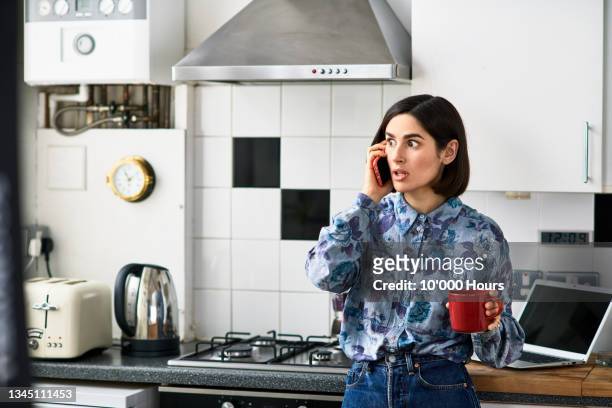 shocked looking woman on phone in kitchen - notfall stock-fotos und bilder