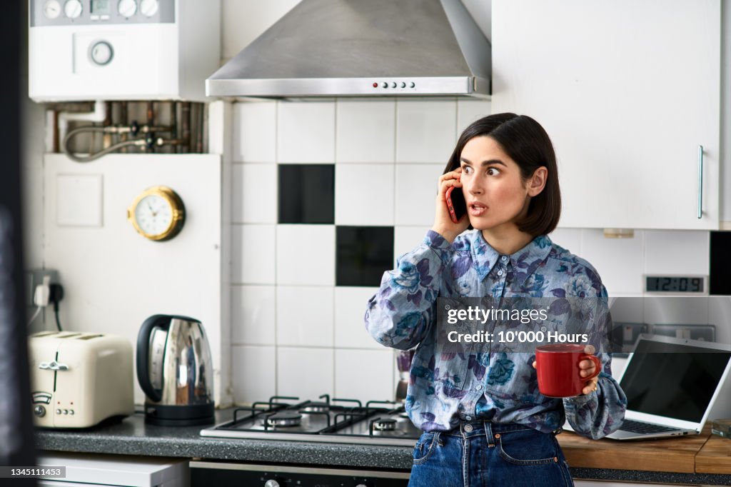 Shocked looking woman on phone in kitchen
