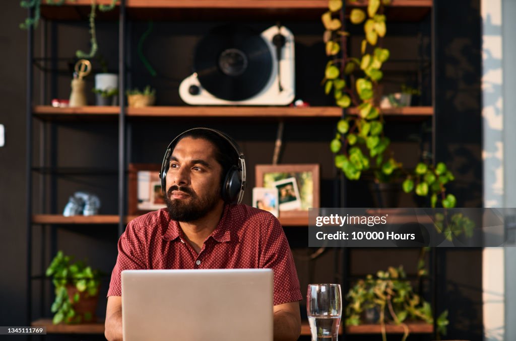 Mid adult man wearing headphones using laptop and looking away