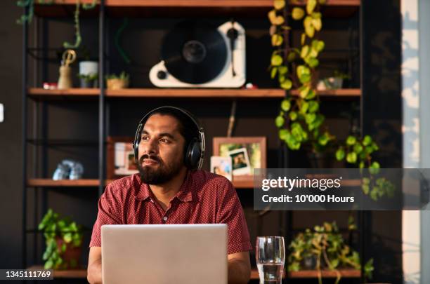 mid adult man wearing headphones using laptop and looking away - business headphones stockfoto's en -beelden