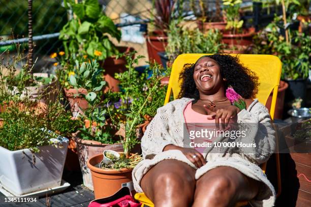 cheerful woman relaxing on deck chair on roof terrace - snapshot of britain stock-fotos und bilder