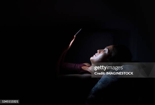 young woman with insomnia looking at her phone at night - smartphone lesen nacht stock-fotos und bilder