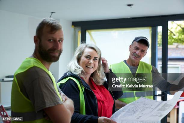 a female  builder laughs whilst examining the building plans with two building workers on a building site. - blond undone bildbanksfoton och bilder