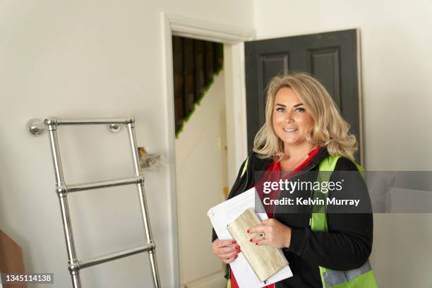 a female  builder stands in a room that is being fully renovated and looks at camera. she holds the plans for the house and smiles. - femalefocuscollection stock pictures, royalty-free photos & images