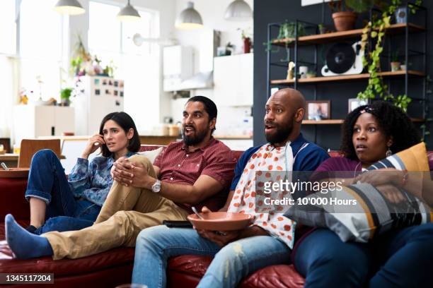 four flatmates watching tv with shocked expressions - escandalo tv fotografías e imágenes de stock