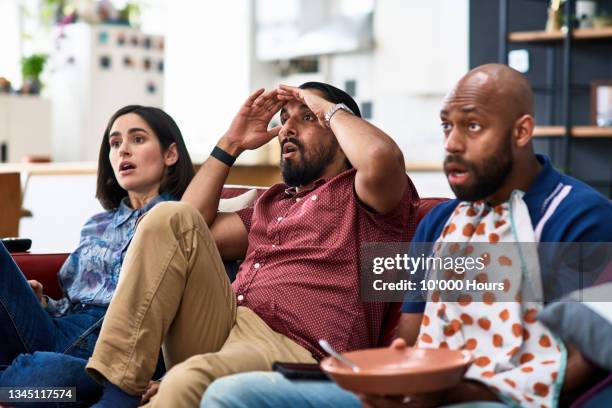 three friends watching tv in disbelief, man with hand on face - reality tv fotografías e imágenes de stock