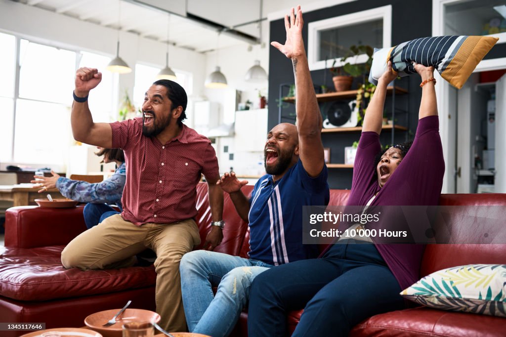 Friends watching TV at home and cheering with arms raised