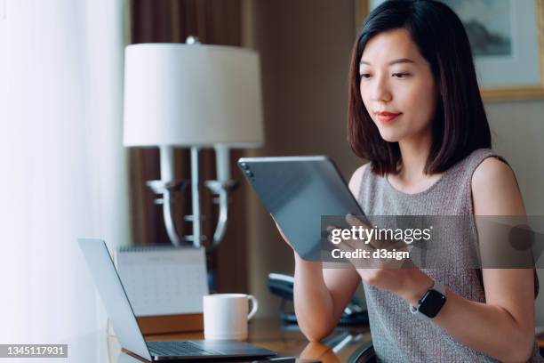 young asian businesswoman using digital tablet while sitting at her desk in office. remote working, freelancer, small business ideas. female leadership. making business connections with technology - woman using digital tablet stock pictures, royalty-free photos & images