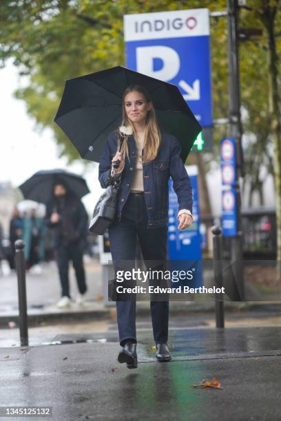 Model wears a black umbrella, a beige ribbed Courreges pullover, a navy blue denim jacket with white sheep collar, a black shiny leather shoulder bag...