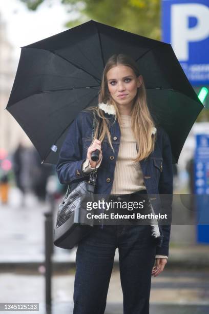 Model wears a black umbrella, a beige ribbed Courreges pullover, a navy blue denim jacket with white sheep collar, a black shiny leather shoulder bag...