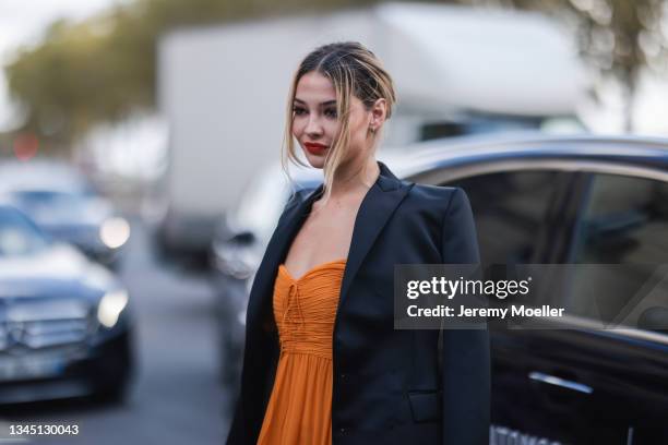 Madelyn Cline wearing orange dress and black blazer outside Giambattista Valli Show on October 04, 2021 in Paris, France.