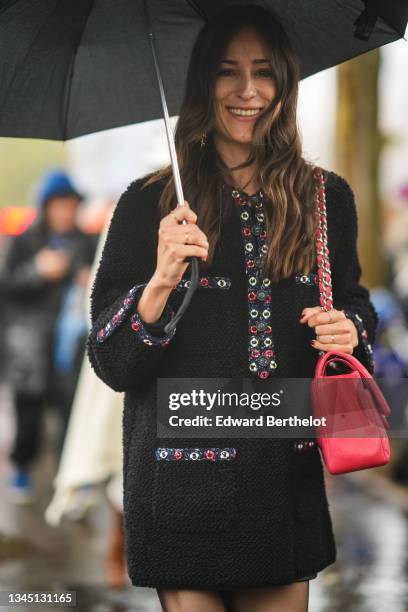 Guest wears a black umbrella, a black tweed long sleeves short dress with red and gold nailed / studded, black tights, a red shiny leather shoulder...