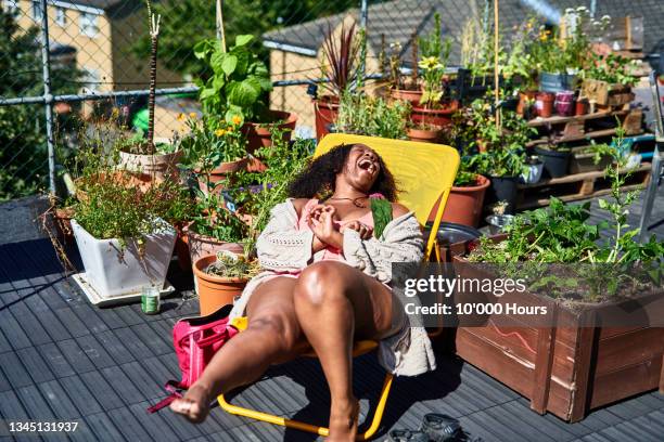 woman laughing on deck chair on roof terrace - dachgarten stock-fotos und bilder