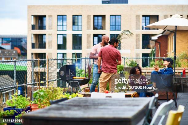 four friends enjoying barbecuing on roof terrace - rooftop bbq stock pictures, royalty-free photos & images