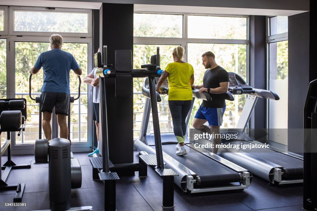Personas mayores que hacen ejercicio en cinta de correr y máquina paso a paso en el gimnasio