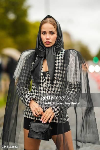Guest wears a black shiny satin scarf, a black and white houndstooths pattern tweed jacket, black shorts, a white and black tulle oversized cloak, a...