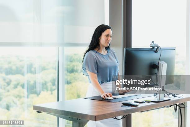 using standing desk, female ceo works in corner office - ergonomie stockfoto's en -beelden
