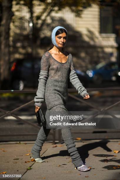 Angela Rozas Saiz wears a blue braided wool hood / balaclava, a gray long V-neck t-shirt, a matching long gray skirt, pale gray ribbed wool gloves, a...