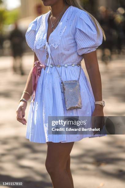 Nina Suess wears silver chain pendant necklaces, a white and baby blue striped puffy sleeves / puffy dress with white lace collar, bracelets, gold...