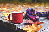 Autumn coffee or tea in a cup on a wooden table against the background of yellow fallen leaves and October weather. Autumn drink, mood and comfort concept.