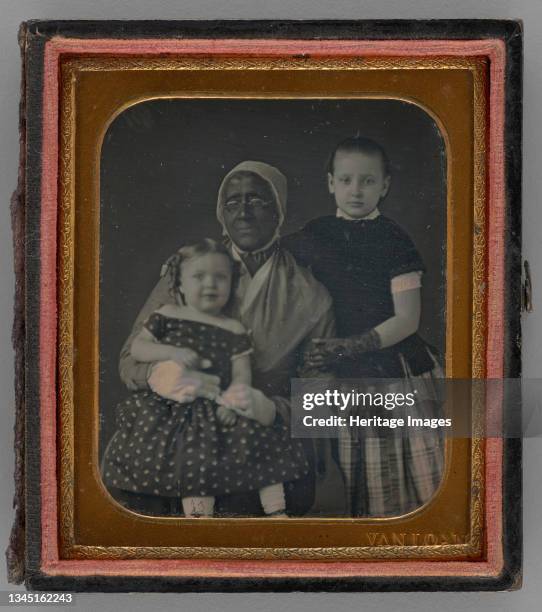 Untitled , 1850s. Black-and-white portrait photograph in gold frame. Black woman with two white children - one on her lap, and the other standing and...