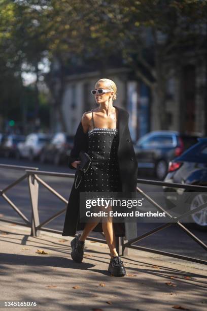 Caroline Daur wears white Prada sunglasses, silver earrings, a black long coat, a black shiny leather embossed pattern Miu Miu handbag, a black...