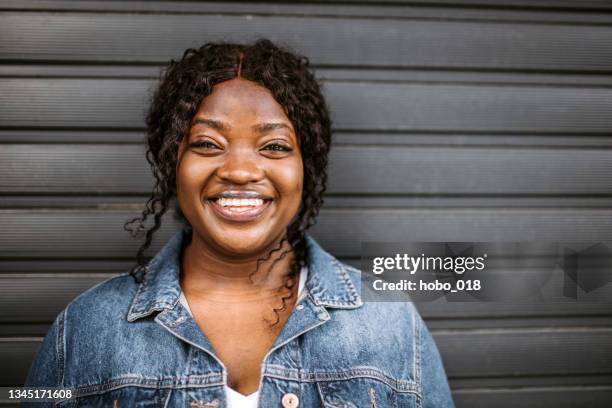 cute black young overweight woman leaning on dark grey garage door - all hip hop models stock pictures, royalty-free photos & images