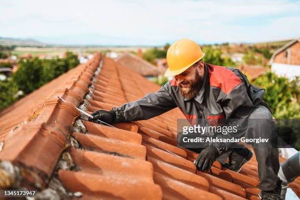 lavoratore barbuto non ha paura dell'altezza mentre misura le piastrelle per la installazione del pannello solare - costruttore di tetti foto e immagini stock