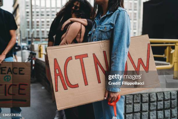 detail of a young adult woman holding a cardboard sign with "act now" words on it - black lives matter stock pictures, royalty-free photos & images