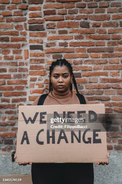 millennial woman is holding a cardboard sign with the text "we need a change" on it - black lives matter stock pictures, royalty-free photos & images