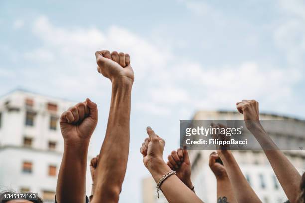 menschen mit erhobenen fäusten bei einer demonstration in der stadt - justice concept stock-fotos und bilder