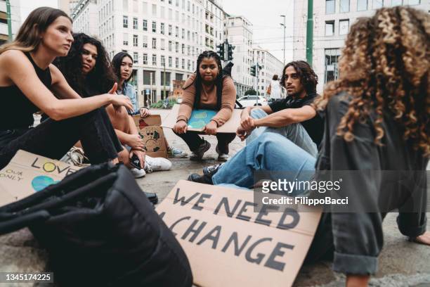 a group of young adult people are resting after a climate change demonstration in the city - environmental protest stock pictures, royalty-free photos & images