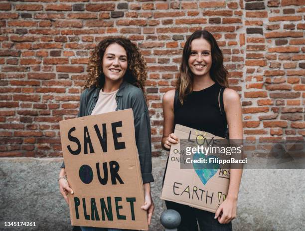 portrait of two young adult women holding cardboard signs against climate change - earth activist stock pictures, royalty-free photos & images