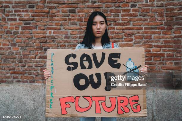 portrait of a chinese young adult woman holding a cardboard sign against climate change - aapi protest stock pictures, royalty-free photos & images