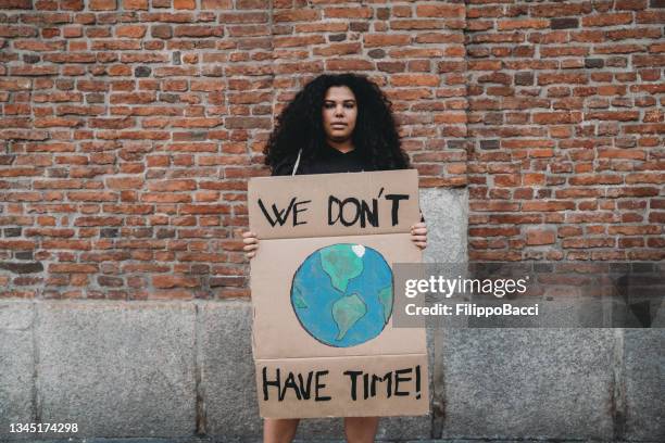 portrait of a young adult woman holding a cardboard sign against climate change - climate change protest stock pictures, royalty-free photos & images