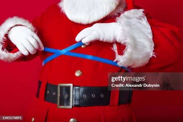 fat santa claus measures himself with a tape close-up on a red background - santa close up stock-fotos und bilder