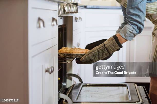mature woman removing fresh baked pie from oven - pie stockfoto's en -beelden