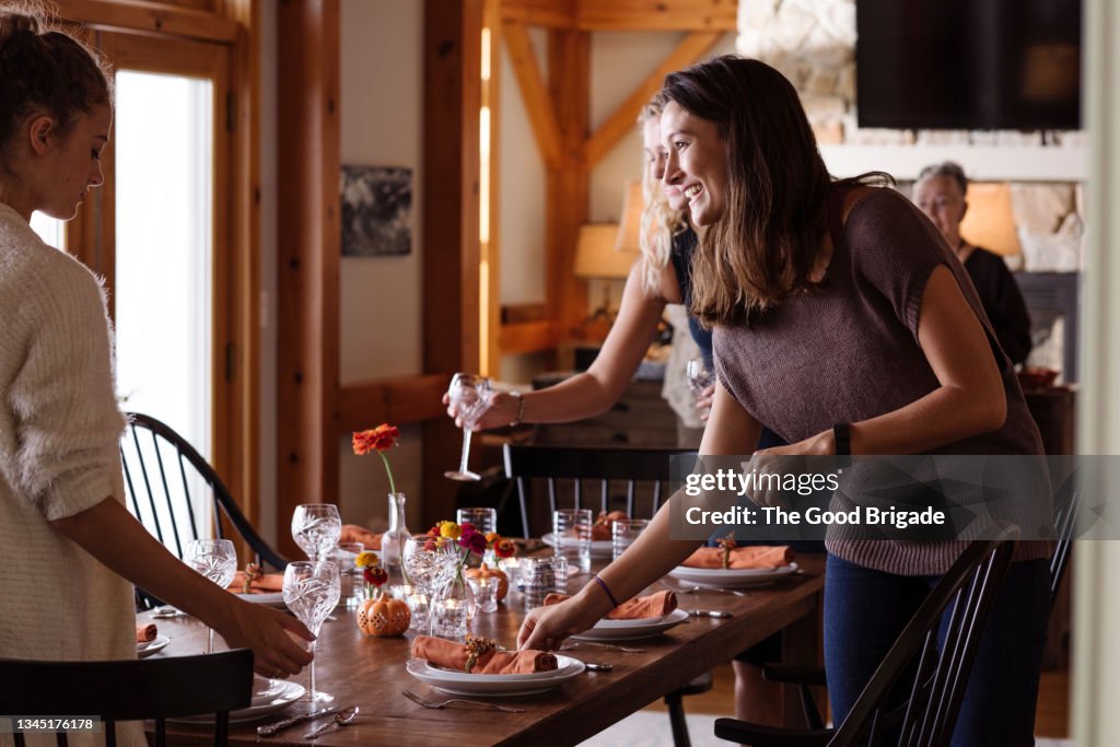 Smiling young woman talking to teenage girl while sitting the table in dining room