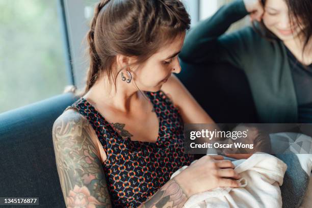 lesbian mothers with newborn daughter on sofa at home - lesbian mom stock pictures, royalty-free photos & images