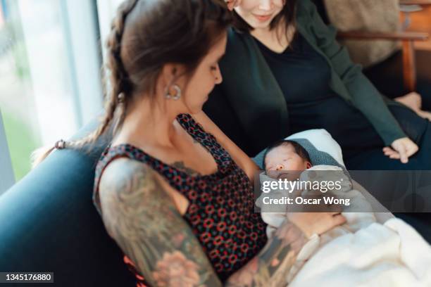 lesbian mothers with newborn daughter on sofa at home - lesbian mom baby fotografías e imágenes de stock