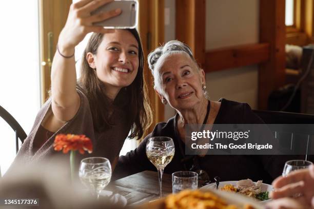 young woman taking selfie through mobile phone with grandmother sitting at dining table - beautiful granny bildbanksfoton och bilder