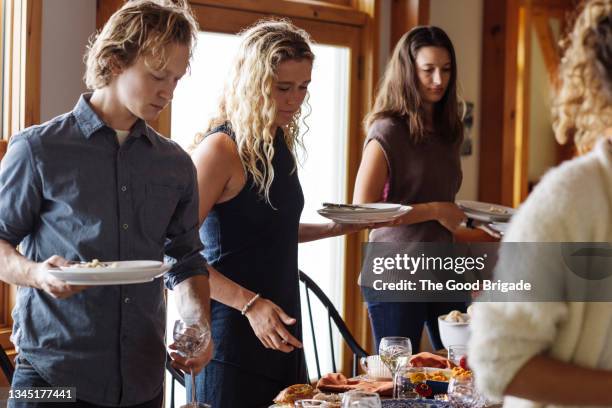 young man and women picking up plates after having thanksgiving at home - thanksgiving plate stock pictures, royalty-free photos & images