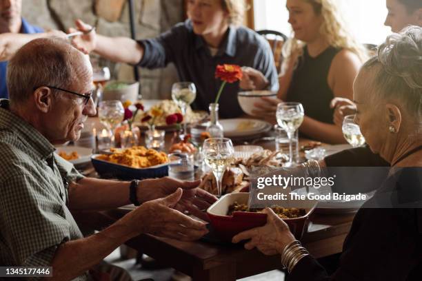 senior man and woman sharing food while sitting at thanksgiving dinner - thanksgiving day stock pictures, royalty-free photos & images